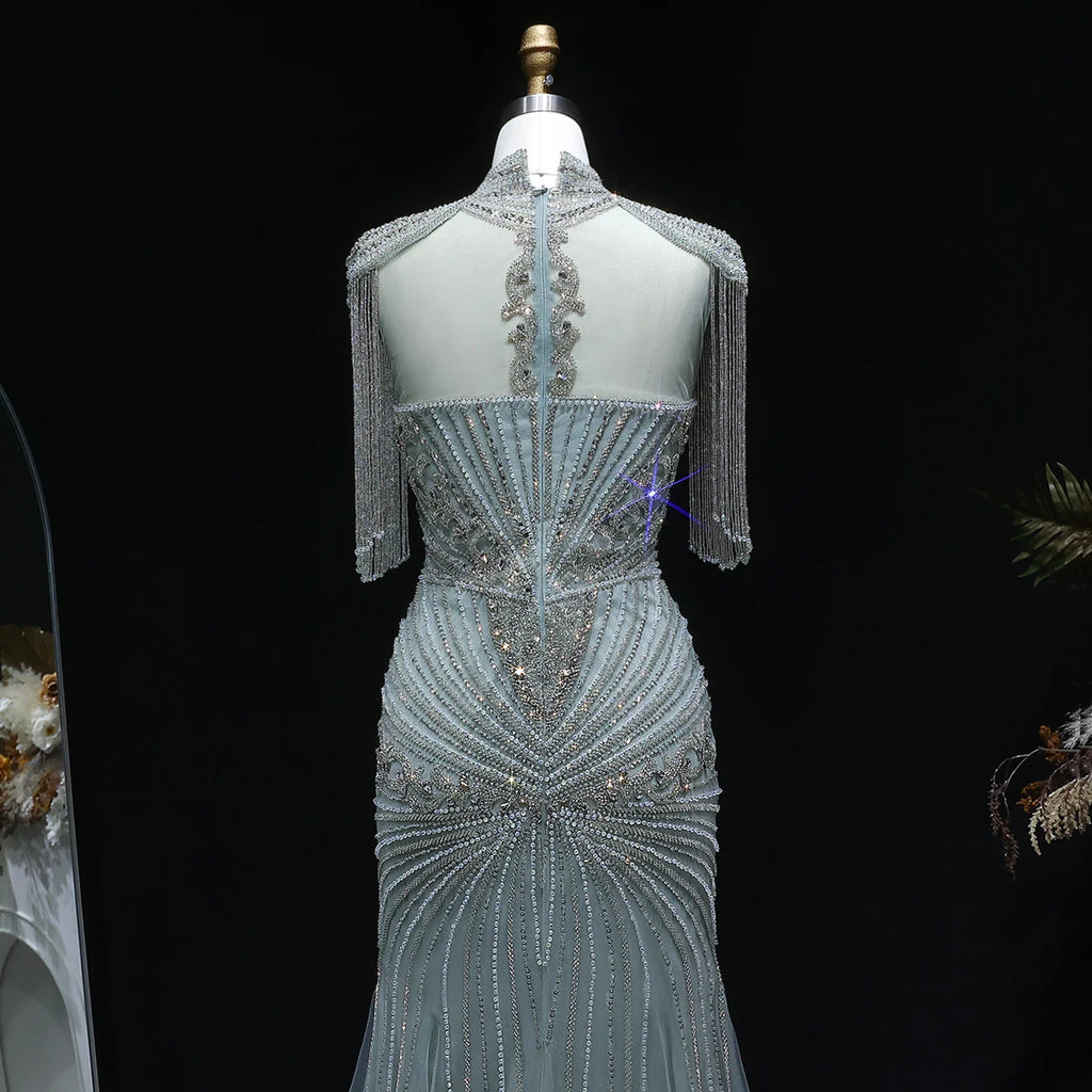 A light blue evening gown with intricate silver beading and fringe details, displayed on a mannequin against a black background.