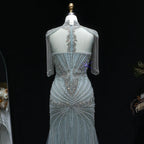A light blue evening gown with intricate silver beading and fringe details, displayed on a mannequin against a black background.