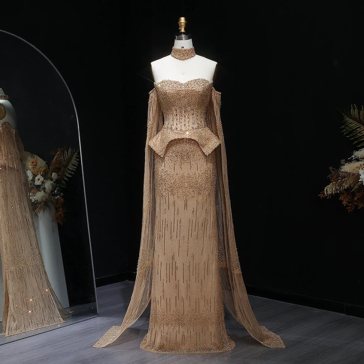 Beige evening gown with cape on a mannequin against a dark background